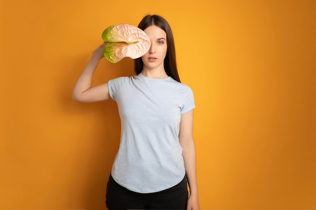 Beautiful woman with hand near face holding anthurium flower on yellow background