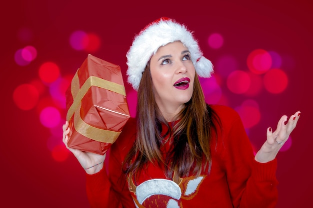 Beautiful woman with hat and Christmas sweater wearing a nice expression with a gift in hand