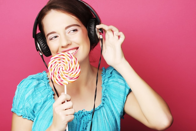 Beautiful woman with headphones and candy on pink