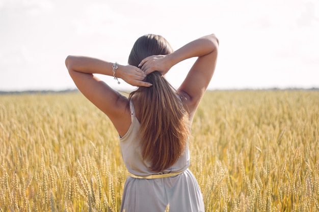 Beautiful woman with healthy long hair back to the camera on rye field