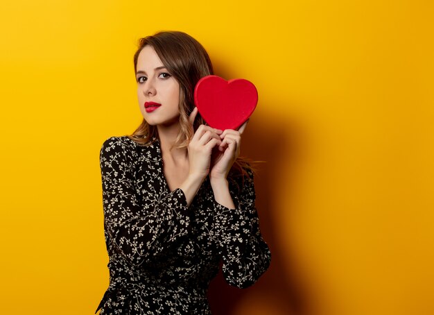 Beautiful woman with heart shape box on yellow wall 