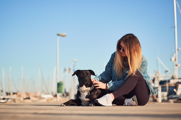 彼女の暗い犬と美しい女性がポートデニムジャケット、夏の日の屋外のポートに座っています。