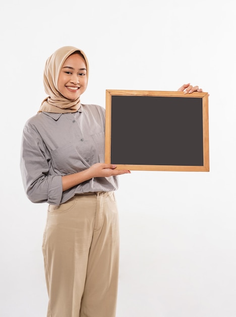 Красивая женщина в хиджабе стоит с улыбкой и показывает доску в руке на белом