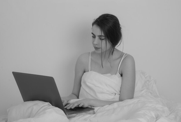 잠 옷에 노트북과 침대 갈색 머리 모델에 노트북과 아름 다운 여자 여자는 컴퓨터에서 작동