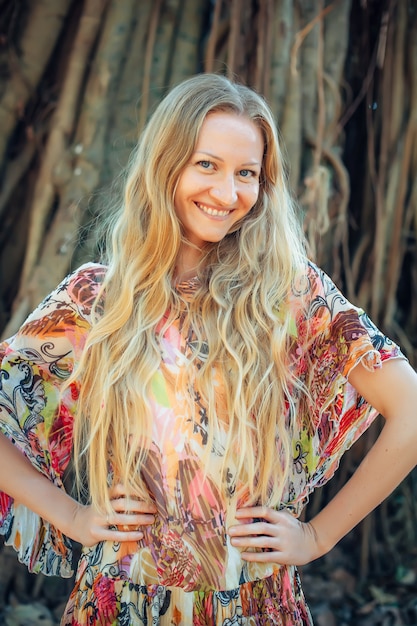 Beautiful woman with long blond hair poses on the background of trees. Portrait of a young long-haired girl.