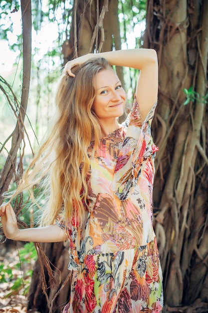 Beautiful woman with long blond hair poses on the background of trees