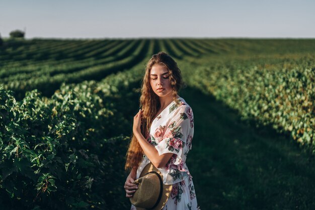 Beautiful woman with long curly hair and freckles face on currant field. woman in a light dress walks in the summer sunny day