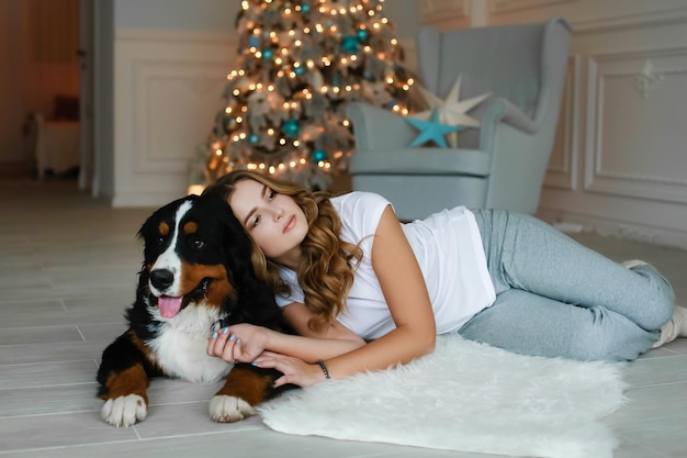 A beautiful woman with long hair lies on a rug against the background of a christmas tree and next t...