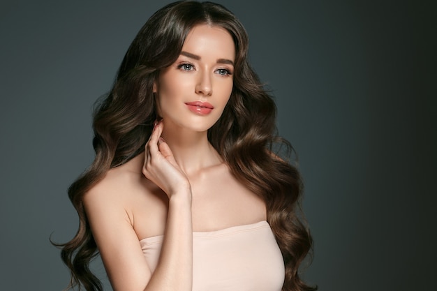 Beautiful woman with long hair, shine and curly, beauty girl female over darl gray background. Studio shot.