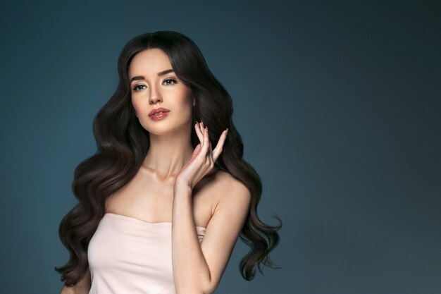 Beautiful woman with long hair, shine and curly, beauty girl female over darl gray background. Studio shot.