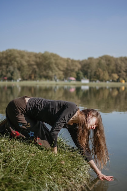 Красивая женщина с длинными волосами касается руками воды озера в солнечный день