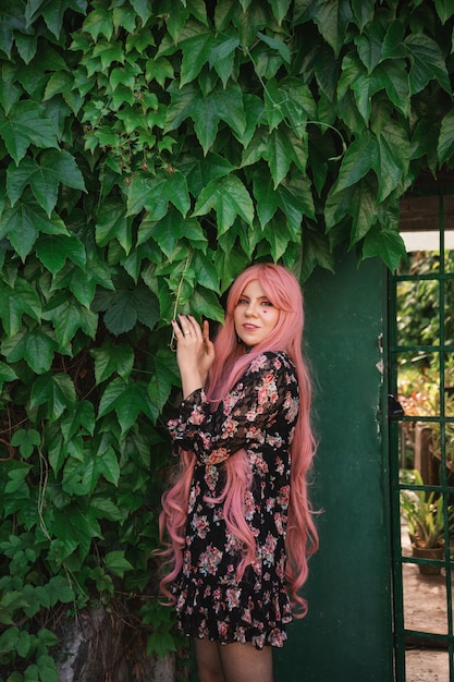 beautiful woman with long pink hair with a top hat and in a black dress stands in the garden