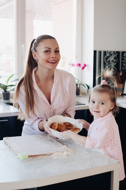 Beautiful woman with lovely child holding bowl with cookies