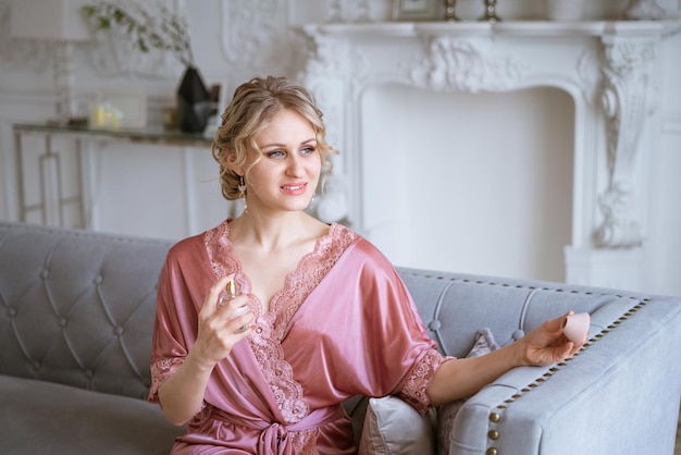 Beautiful woman with makeup and hairstyle in pink silk robe sprinkles perfume