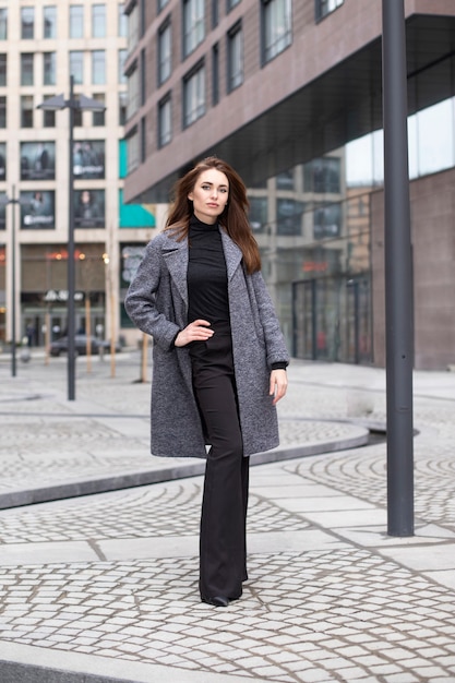 Beautiful woman with makeup in a spring coat and trousers posing on the city streets. Woman in formal clothes smiling cute