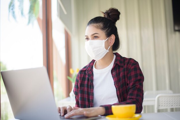 La bella donna con la maschera sta lavorando al computer portatile del computer in caffetteria