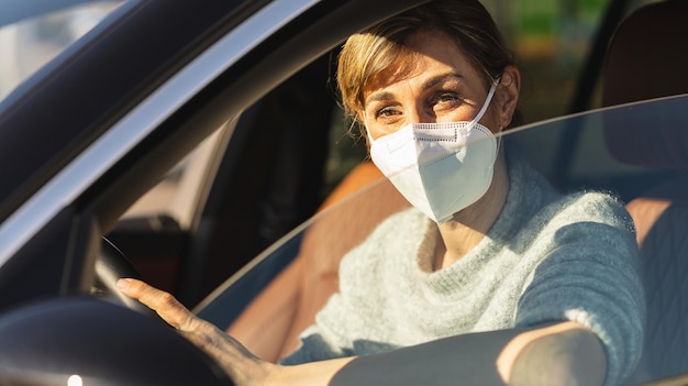 Bella donna con una maschera antivirus n95 ffp2 seduta in una maschera protettiva per auto contro il conducente del coronavirus in una strada cittadina durante un focolaio di coronavirus covid19