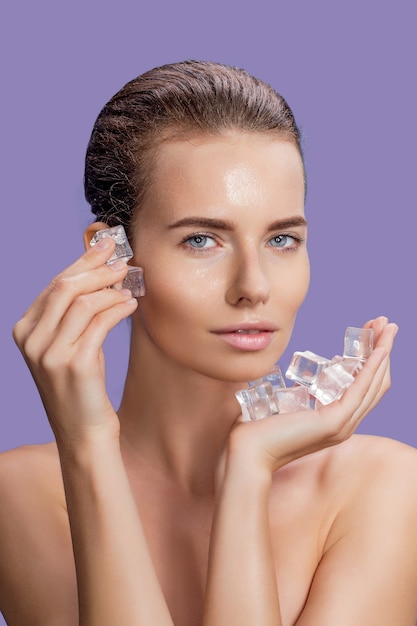 Beautiful woman with natural looking makeup holding ice cubes near face