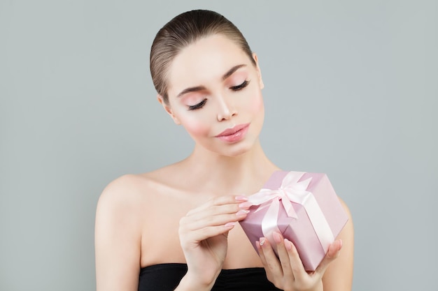 Beautiful Woman with Perfect Skin, Makeup and Manicure Holding Gift Box with Pink Silk Ribbons. Surprise