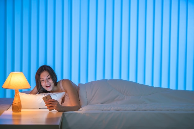 The beautiful woman with phone lay on the bed. Evening night time