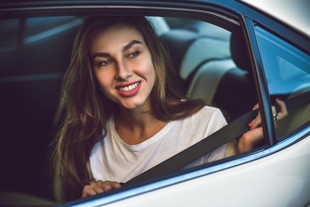 車の後部座席に座って笑顔の電話を持つ美しい女性。