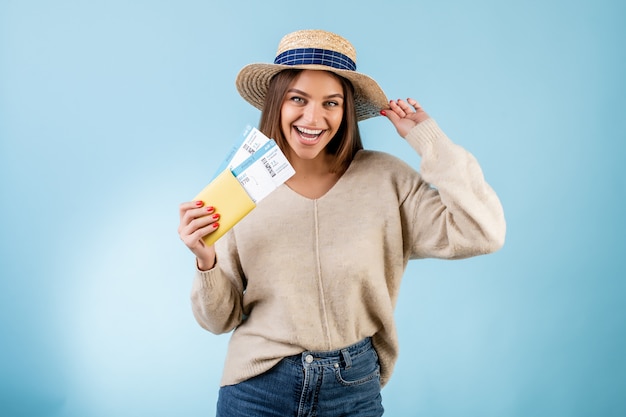 Красивая женщина с билетами на самолет в паспорте и дорожной шляпе, изолированных на синем