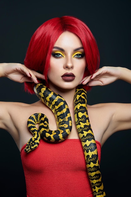 Beautiful woman with red hair and a yellow python snake around\
her neck. professional bright beauty eye makeup yellow, red\
burgundy lipstick