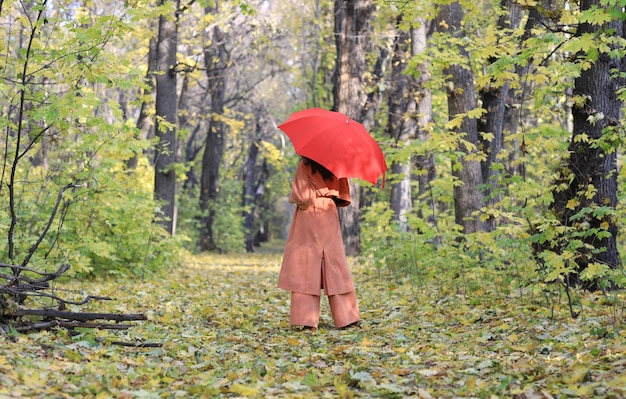 Красивая женщина с красным зонтиком в осеннем лесу