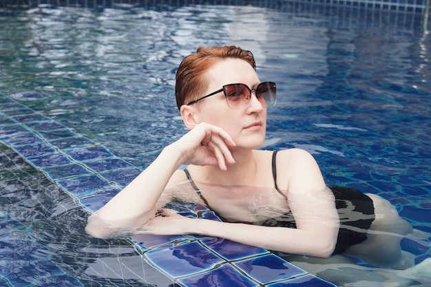 Beautiful woman with short red hair is relaxing in the pool