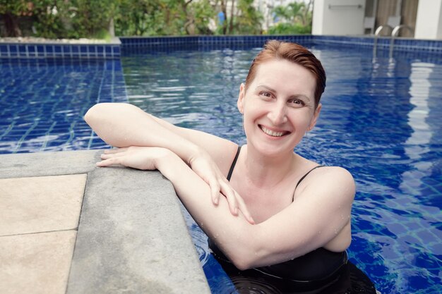 短い赤い髪の美しい女性がプールでリラックスしています。