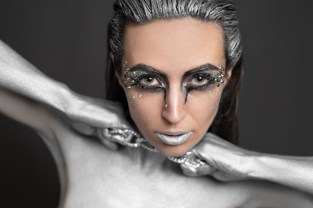 Beautiful woman with silver paint on her skin and hair breaks the chain around her neck.