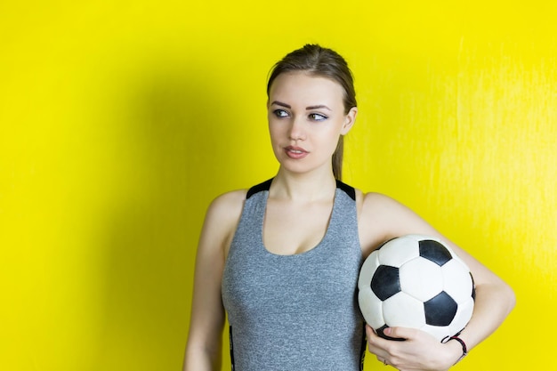 Beautiful woman with soccer ball standing against yellow background