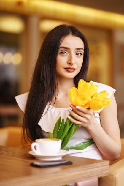 Beautiful Woman With Spring Tulips Flowers Bouquet At Cafe Woman Drinking Coffee And Using Phone