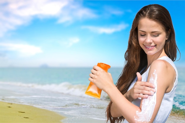 Красивая женщина с кремом солнцезащитный крем солнечной над предпосылкой океана. Солнечный загар.