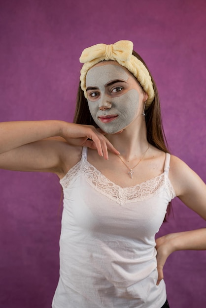 보라색에 고립 된 치료 녹색 점토 얼굴 마스크를 가진 아름다운 여성