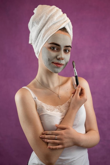 Beautiful woman with therapeutic green clay facial mask isolated on purple