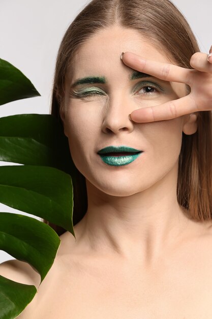 Beautiful woman with unusual makeup and tropical leaf on white background