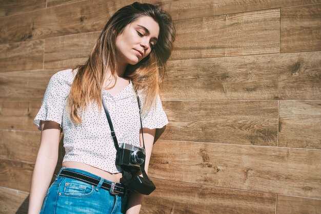 Beautiful woman with vintage old camera standing at a wood wall