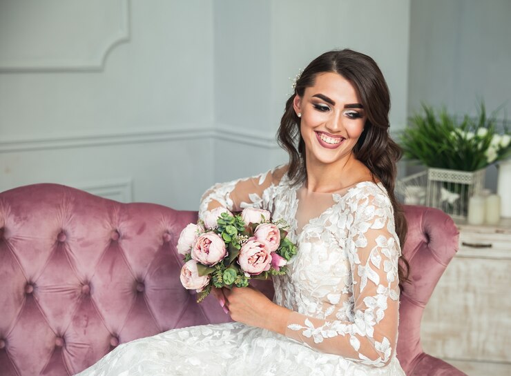 Beautiful woman with wedding makeup, dress and jewelry wreath on long curly hair. Attractive young bride portrait. Bridal fashion model posing in interior. Sensual lady. Hairstyle, beauty, flower