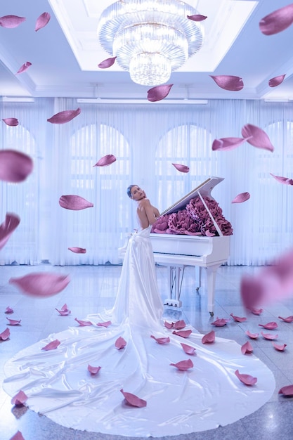 Beautiful woman with white piano and peonies flowers in white studio