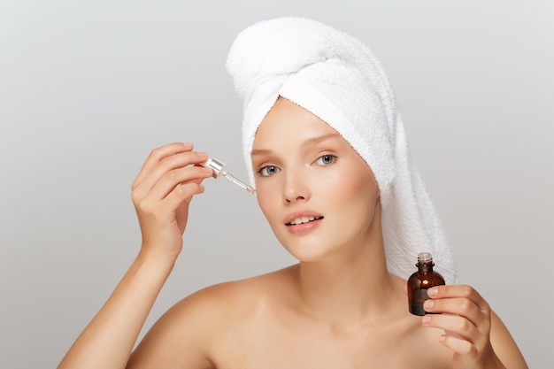 Beautiful woman with a white towel and a serum bottle