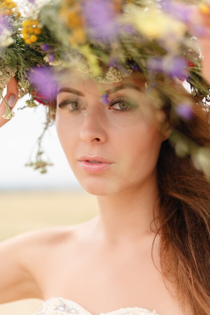 花のフィールドに座っている彼女の頭に花輪を持つ美しい女性。美しさ、自由な生活、自然の概念