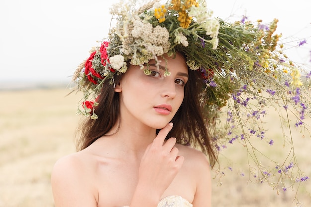 花のフィールドに座っている彼女の頭に花輪を持つ美しい女性。美しさ、自由な生活、自然の概念