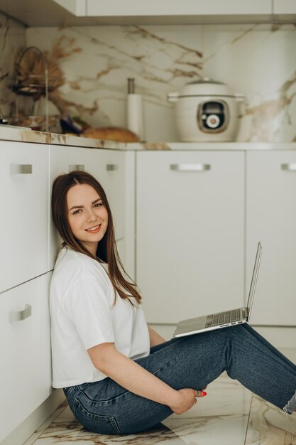 Beautiful woman working with laptop sitting on the floor in the kitchen