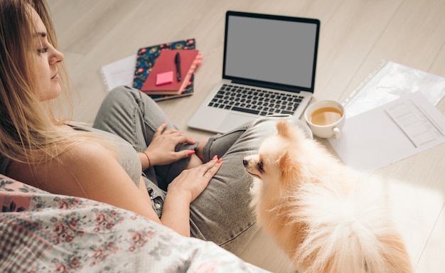 Beautiful woman works from home. The dog helps her. Pomeranian spitz sits nearby.