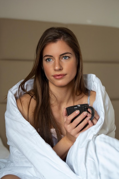Beautiful woman wrapped in a blanket after waking up entering a\
day with cup of coffee happy and relaxed after good night sleep\
sweet dreams good morning new day weekend holidays concept