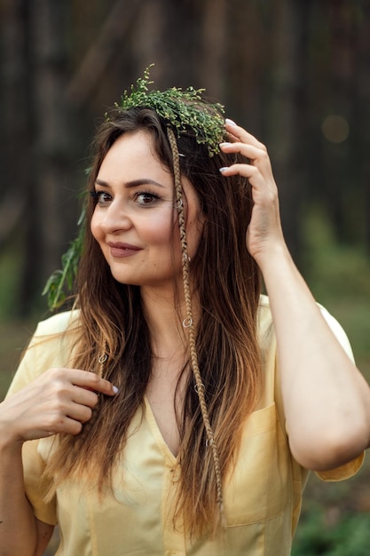 Beautiful woman in wreath of herbs and flowers in forest on sunny day Portrait of candid woman wearing a wreath of wild flowers Midsummer Earth Day