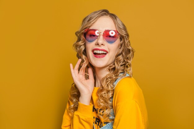 Beautiful woman in yellow sweatshirt and sunglasses on bright background