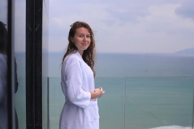 바다 또는 바다 전망이 있는 옥상에 있는 스파 럭셔리 호텔에서 흰색 목욕 가운을 입은 아름다운 여성 어린 소녀는 휴식을 취하고 휴가를 즐기며 웃고 있는 섬