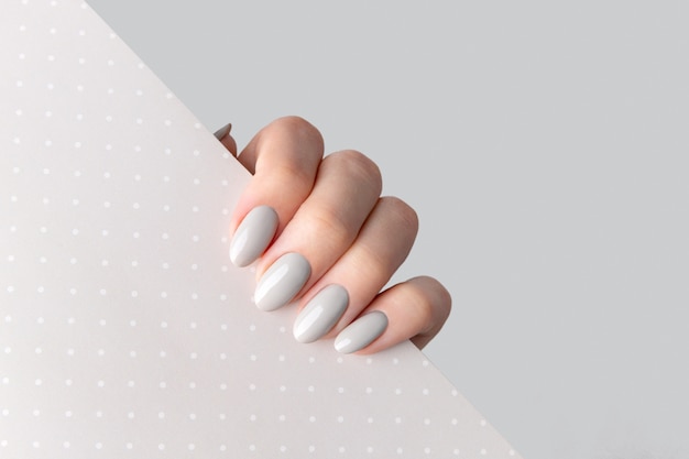 Beautiful womans hand with manicure close up on polka dot background. Gray nail polish